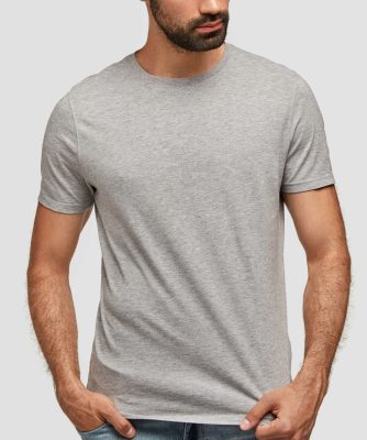 Studio shot of fashionable young bearded male in oversized grey t shirt and jeans, poses indoors against blank wall for your advertisement or promotional text. People, fashion and design concept